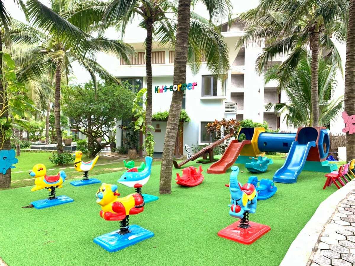 Children&rsquo;s playground with colourful slides and spring riders on artificial grass beside a white building