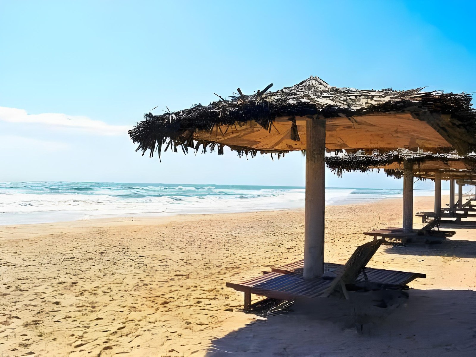 Thatched beach umbrellas and wooden loungers on a wide sandy beach with calm blue sea