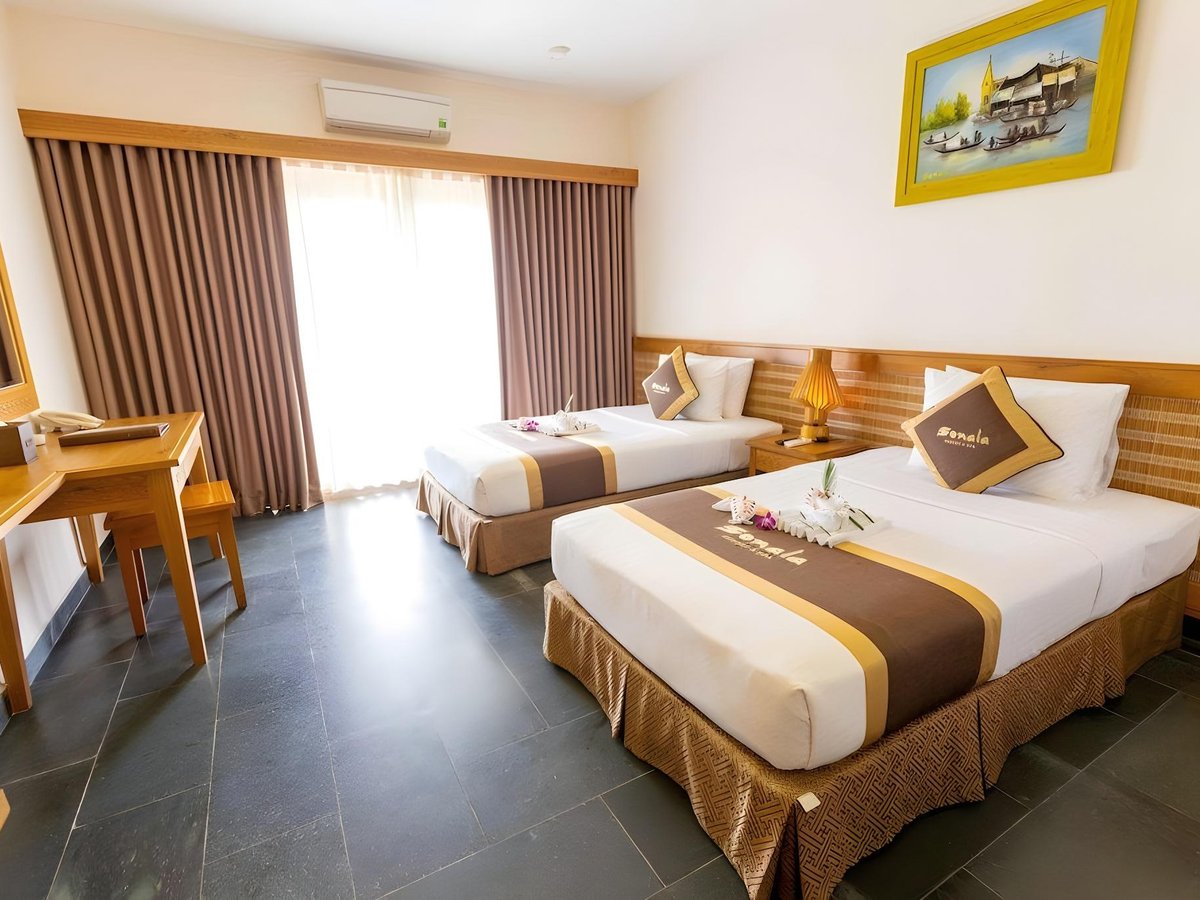 Phòng hai giường đơn trải khăn trang trí nâu vàng, sàn lát gạch sẫm màu và bức tranh phía trên đầu giường